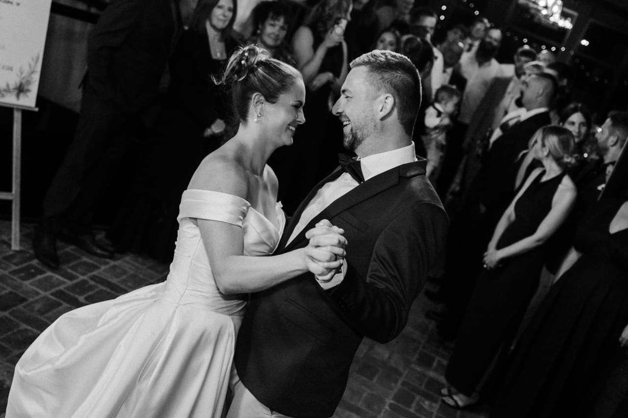 Black and white photo of a couple dancing close together surrounded by their guests