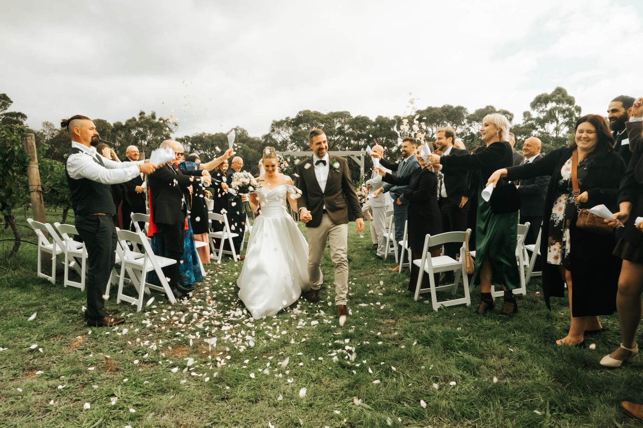 A couple walking through a shower of petals between rows of guests