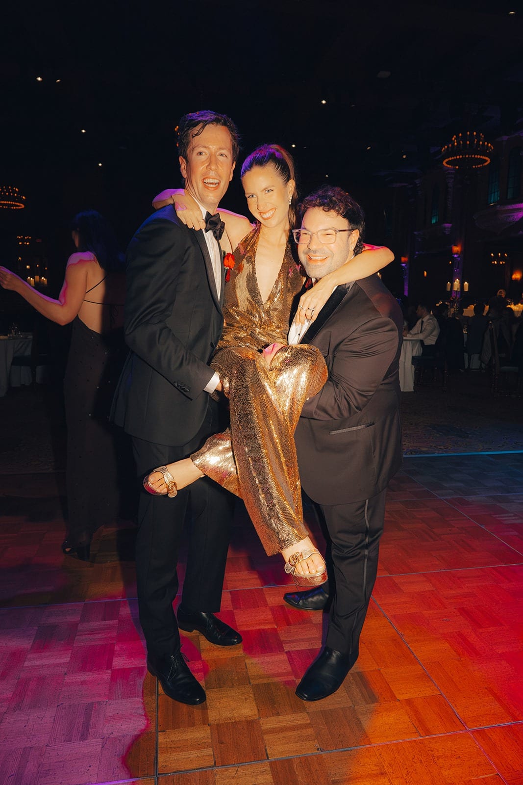 Nick and a friend holding Kira up between them on the dance floor